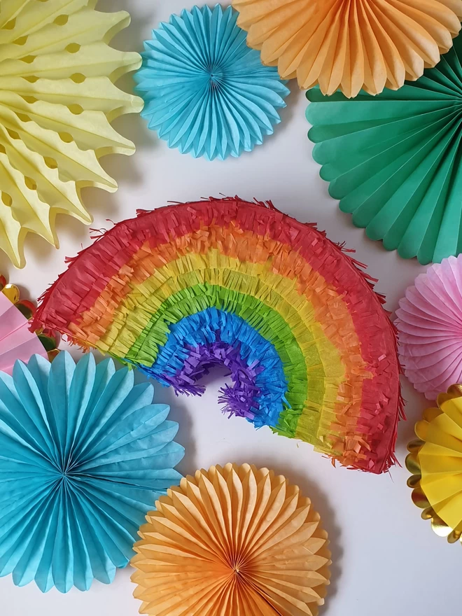front on view of a rainbow pinata surrounded by paper fan decorations