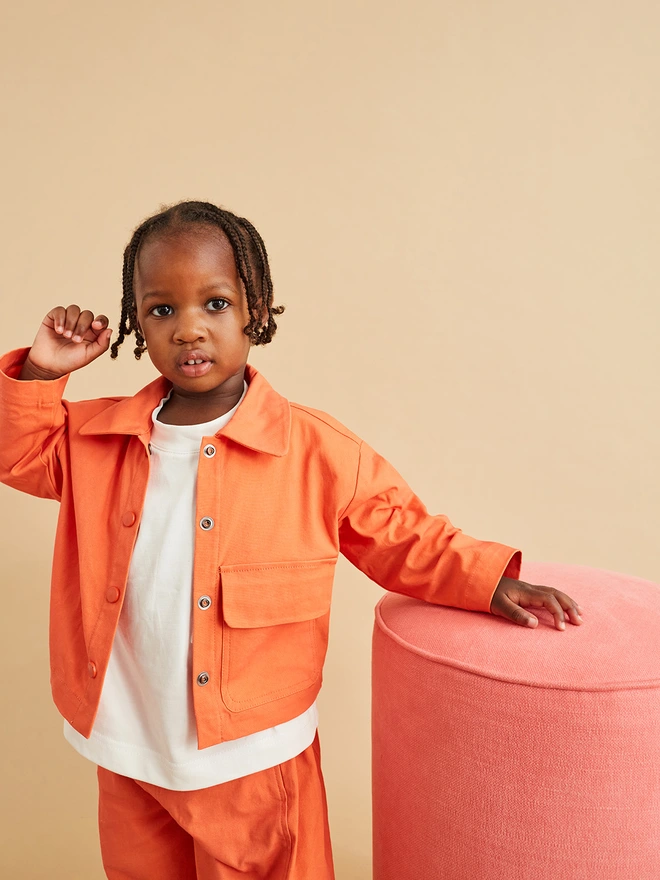 cool boy model photographed by leonie freeman, child wearing matching orange coord unisex kids girl jacket and orange oversize trousers