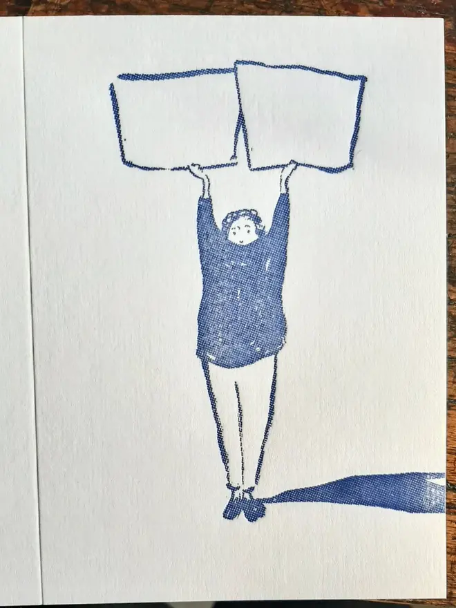 Blank Message Letterpress Handprinted Greetings Card, a white greetings card with a blue design, sitting against a wooden background. 