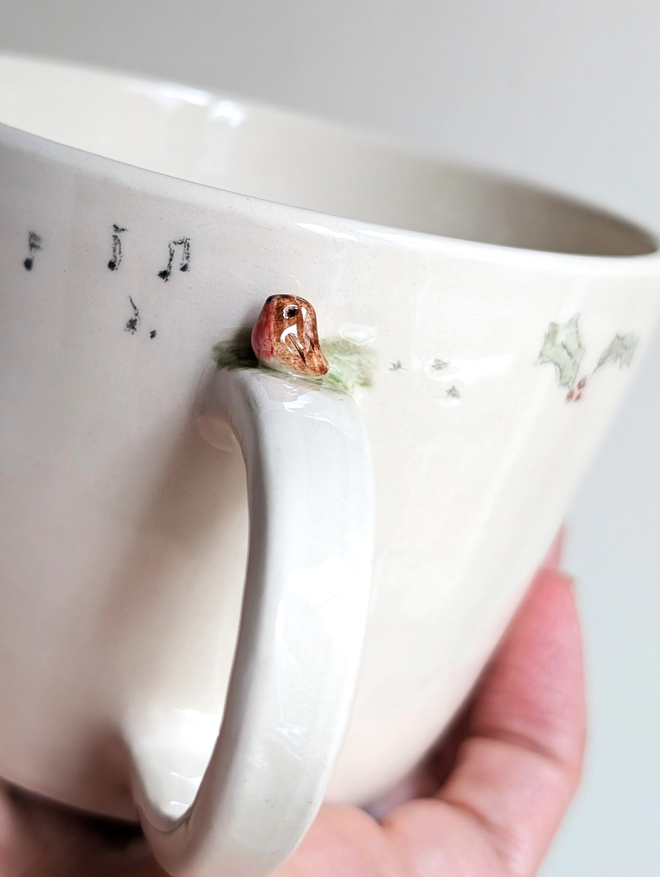 ceramic cup with a tiny pottery robin on the handle with musical notes hand painted christmas holly and tiny bird prints