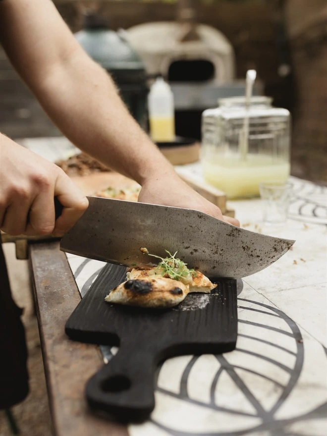 Cutting focaccia on round handled  charred black board