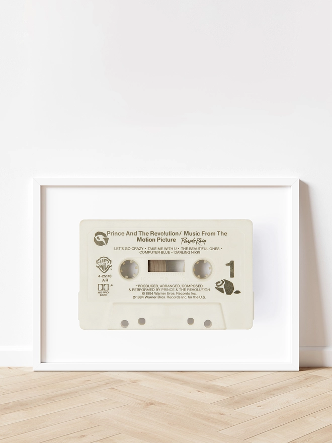 prince purple rain cassette tape print. framed print propped up against white wall and wooden floor.