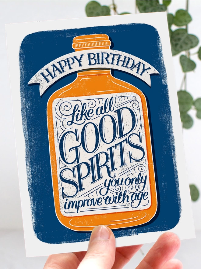 good spirits birthday card held in left hand with leaves in background