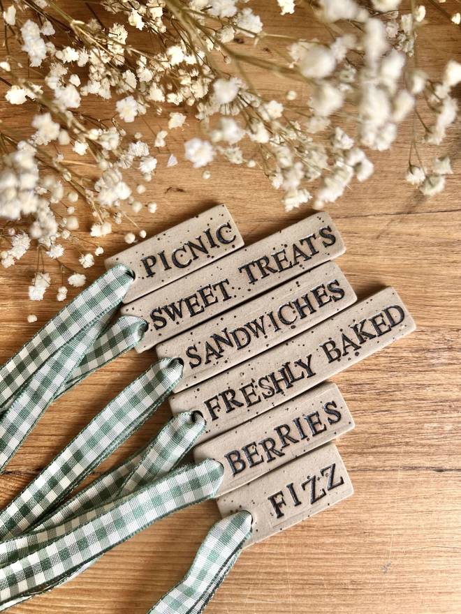6 ceramic tags embossed with picnic themed phrases and strung with green gingham ribbon