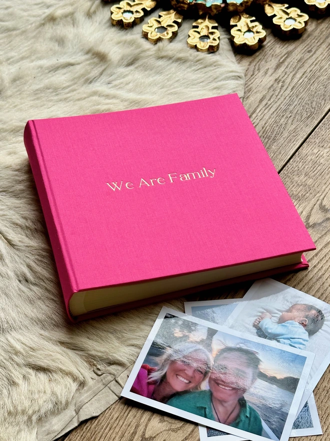 a pink photo album is on a rug and it has been surronded by photos of friends and family.