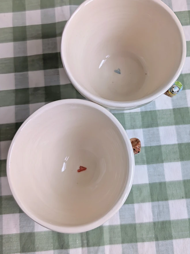 robin and blue tit espresso coffee cups with a tiny handmade bird resting on a small ceramic wooden tree branch in white earthenware pottery shown from above with a small red or blue heart inside