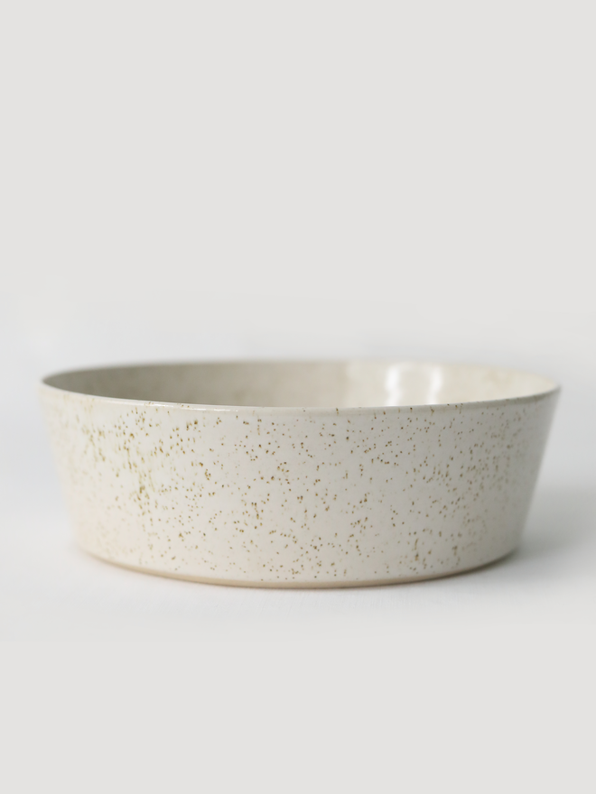 A single wide, shallow glazed ceramic pasta bowl in pepper white, photographed from a slight angle against a plain light grey background, showing the unglazed natural clay base.