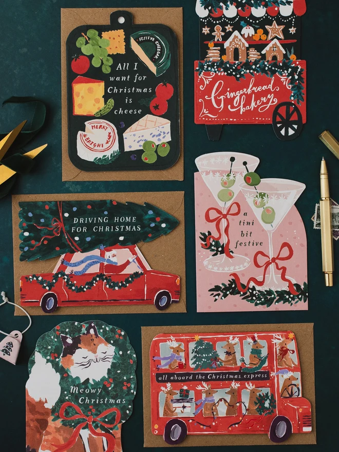 Driving Home For Christmas card on a dark teal background with the Cheeseboard, Gingerbread Cart, Tini Bit Festive and reindeer bus cards