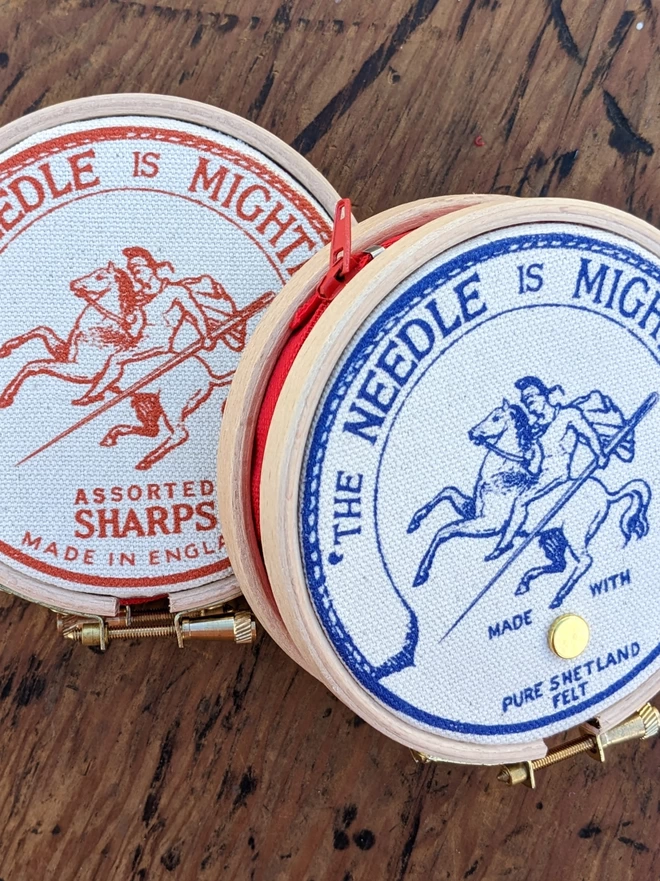 Two needle books in orange and two 'the needle is mightier' embroidery hoop needle books depicting a soldier on horse back with a needle as a sword