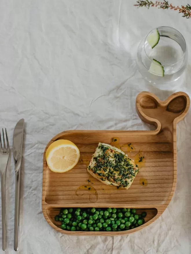 Wooden whale plate with fish, peas and lemon in a birdseye view