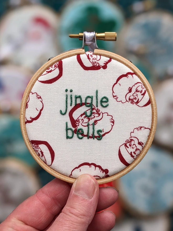 A hand embroidered hoop on Christmas fabric reading jingle bells