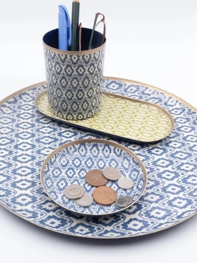 Large Enamel Circular Tray. A blue ikat-patterned pen pot, green oval tray and small coin dish arranged on a large matching round tray. The coordinated desk set keeps pens, glasses and loose change neatly organised.