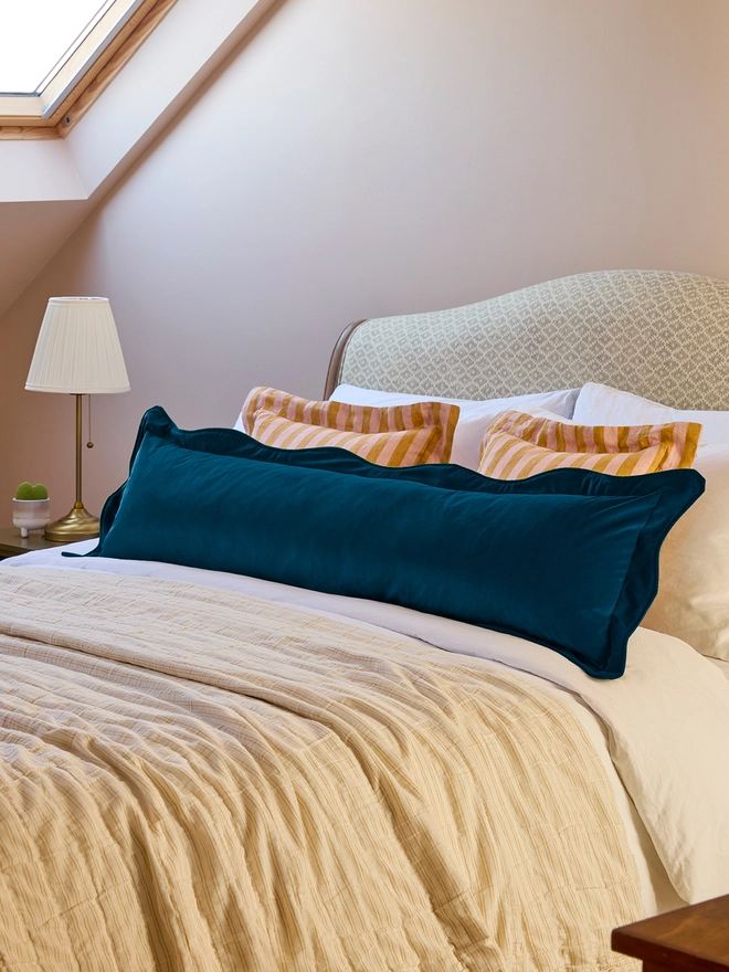 Handmade scalloped teal velvet bolster cushion 130cm with feather pad paired with stripe linen cushions on bed, Kika Bespoke