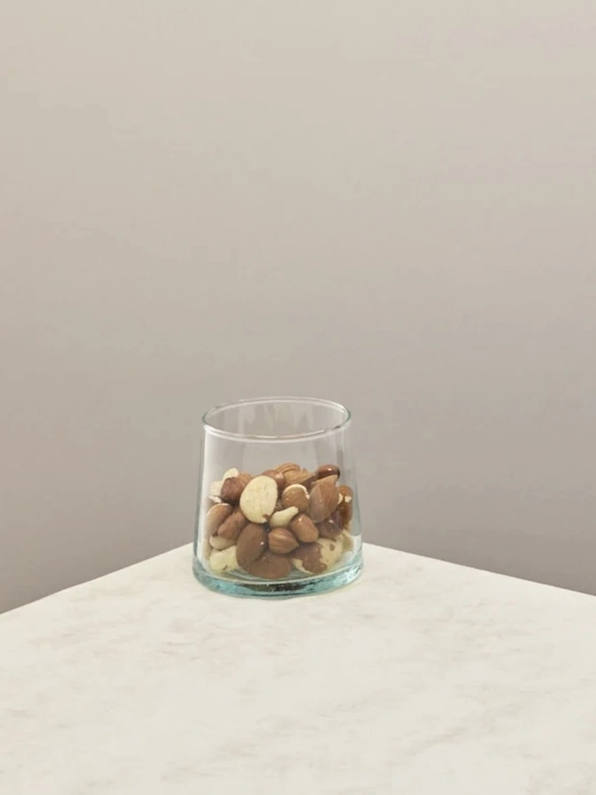 Low Glasses (Set Of 1 Or 4), a low glass sitting on a white counter top against a plain backdrop. It is filled by a some nuts.  