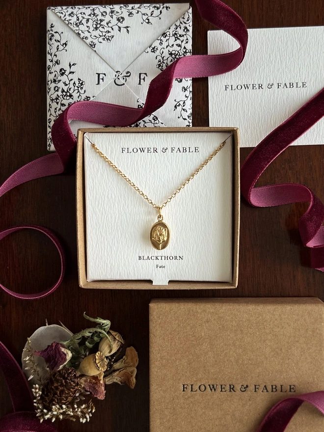 Gold blackthorn medal charm on a belcher chain necklace with flower & fable packaging on a darkground