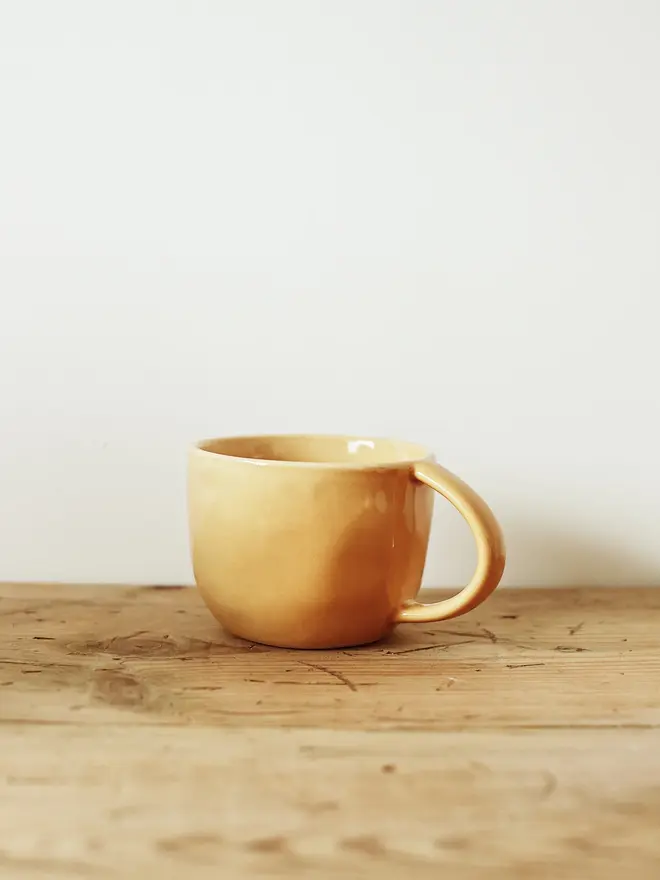 handcrafted stoneware mug. a yellow stoneware mug on a wooden bench.