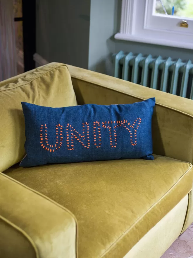 Her Story Cushion - UNITY seen on a yellow velvet sofa.