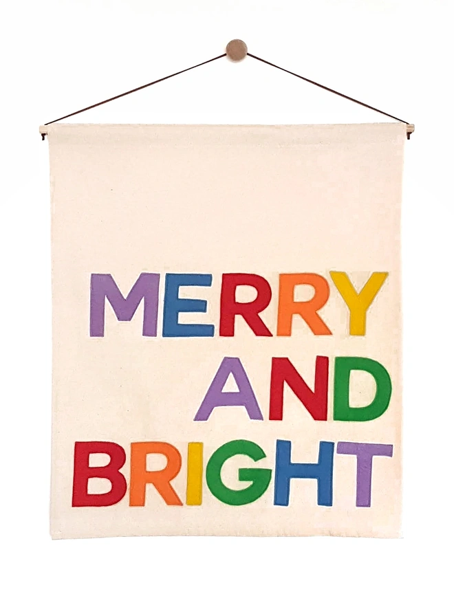 Merry and Bright stitched onto a fabric wall hanging in bright rainbow colours