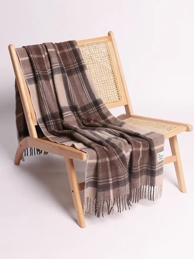 Stewart Natural Dress Blanket, a brown blanket draped over a wooden chair on a white surface against a plain backdrop. 