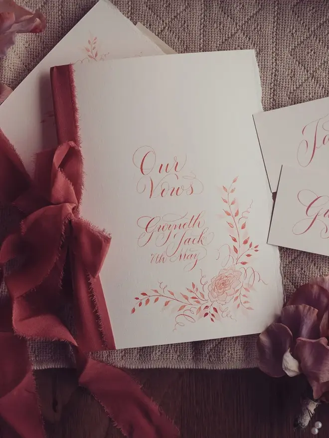 personalised calligraphy wedding vow booklet. white booklet with rust red calligraphy on cover.