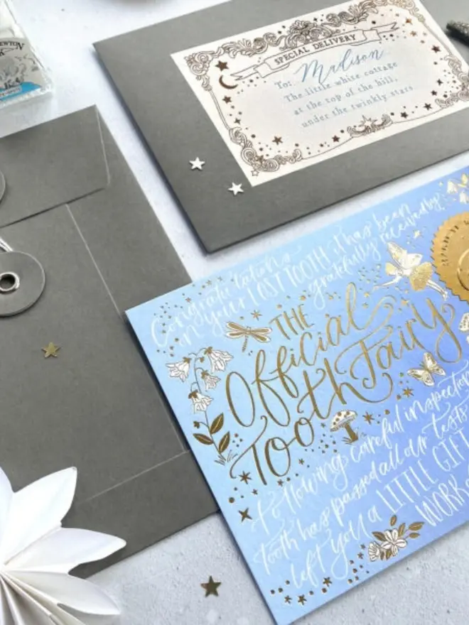 The blue notecard lies next to grey envelopes, one with a "Special Delivery" label addressed to Madison. Gold foil dragonflies, bluebells and butterflies decorate the card.