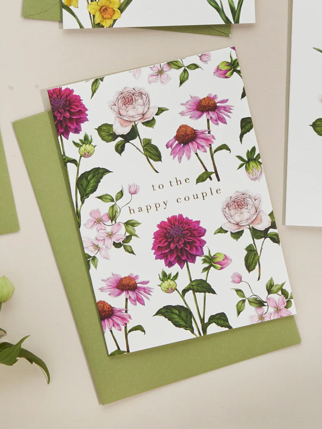 'to the happy couple' illustrated floral card. a white floral card and green envelope photographed against a plain background.