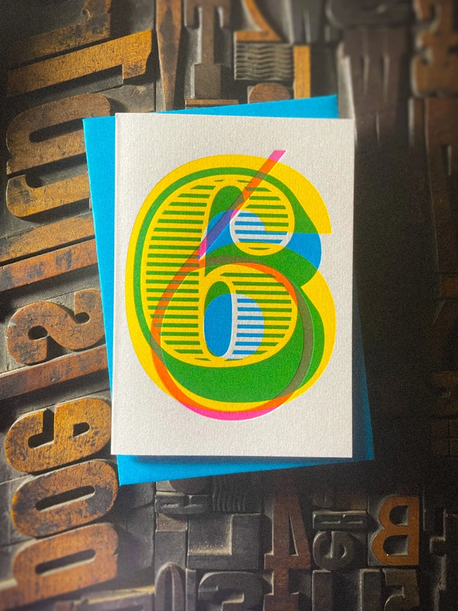 Handmade letterpress 6th birthday card featuring bold overlapping numerals printed in vibrant fluorescent cyan, magenta and yellow inks. Each card is individually hand printed using traditional letterpress techniques on luxury paper stock, creating a beautifully tactile finish with a deep impression and rich layered colours inspired by the CMYK printing process. Printed on a traditional letterpress from 1915.