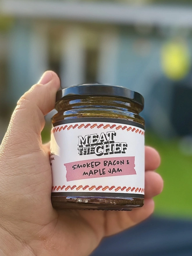 Smoked Bacon & Maple Jam (Set Of 1, 2 Or 3), a person holding a jar of jam outside in their hands. 