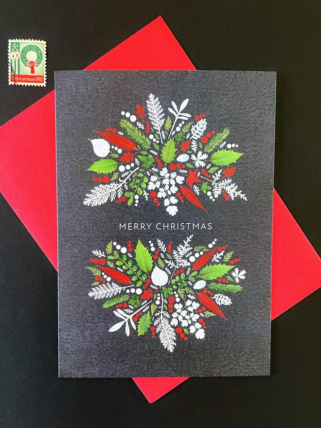 Digitally printed Christmas card with red, white and green pressed leaves, including Holly and Ivy, on dark charcoal desktop with red envelope