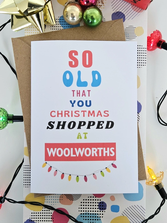 A photograph of the front of a humorous A6 greeting card illustrated using brightly coloured text and the retro shop logo. The text says so old you Christmas shopped at Woolworths with a string of fairy lights