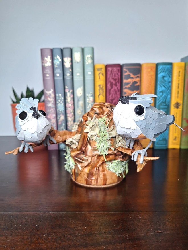 Handmade paper sculpture depicting two tufted titmice perched on a tree stump