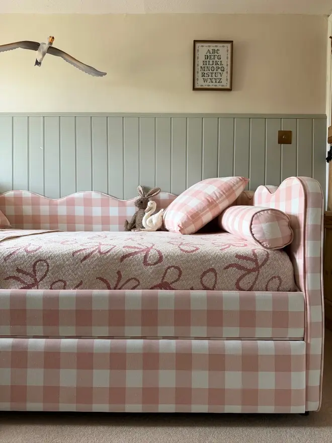 'The Lochlan' upholstered gingham trundle bed. a pink gingham children's sofa-style bed with cushions and a duvet.