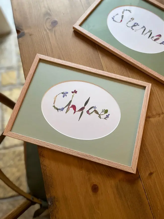 Personalised Original Pressed Flower Name In Frame, a pair of framed flower name prints sitting  on a wooden surface. 