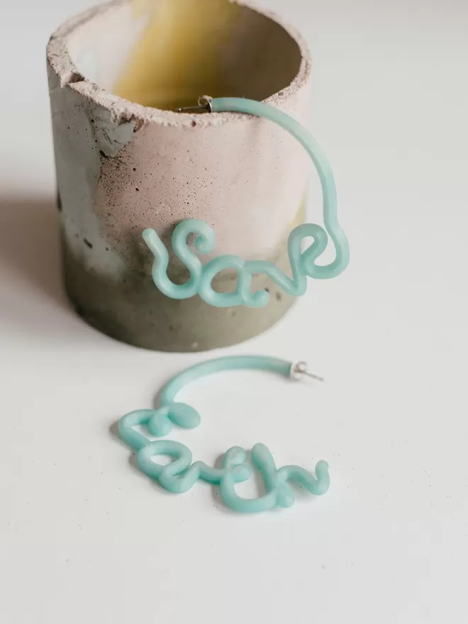 100% Recycled Ocean Plastic - 'Save' 'Earth' Hoop Earrings seem in an earthy cup.