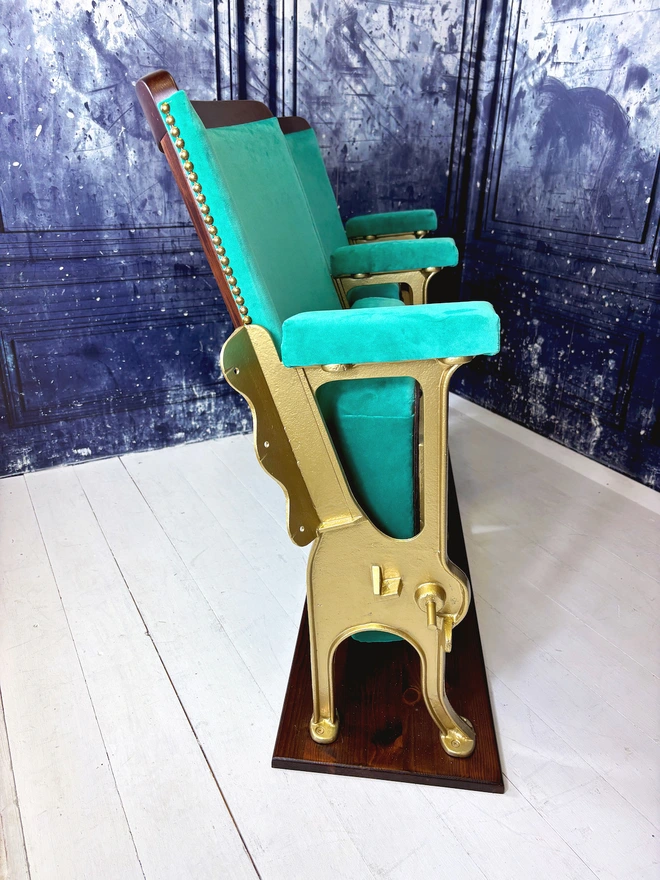 Side view of a set of two vintage refurbished cinema seat upholstered in a beautiful green plain velvet.  The cinema seats have gold legs and are mounted onto a wood plinth.