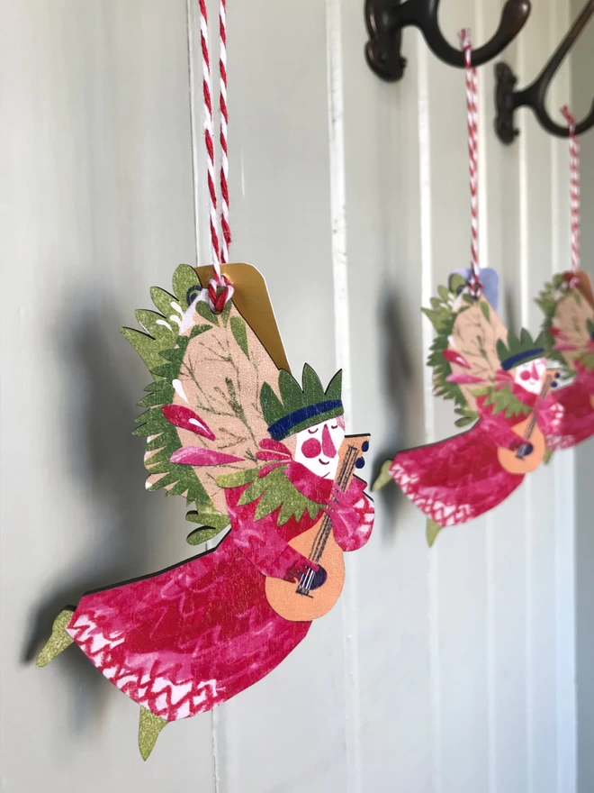 Red and green illustrated angel decoration by Esther Kent, hangs from red and white striped string