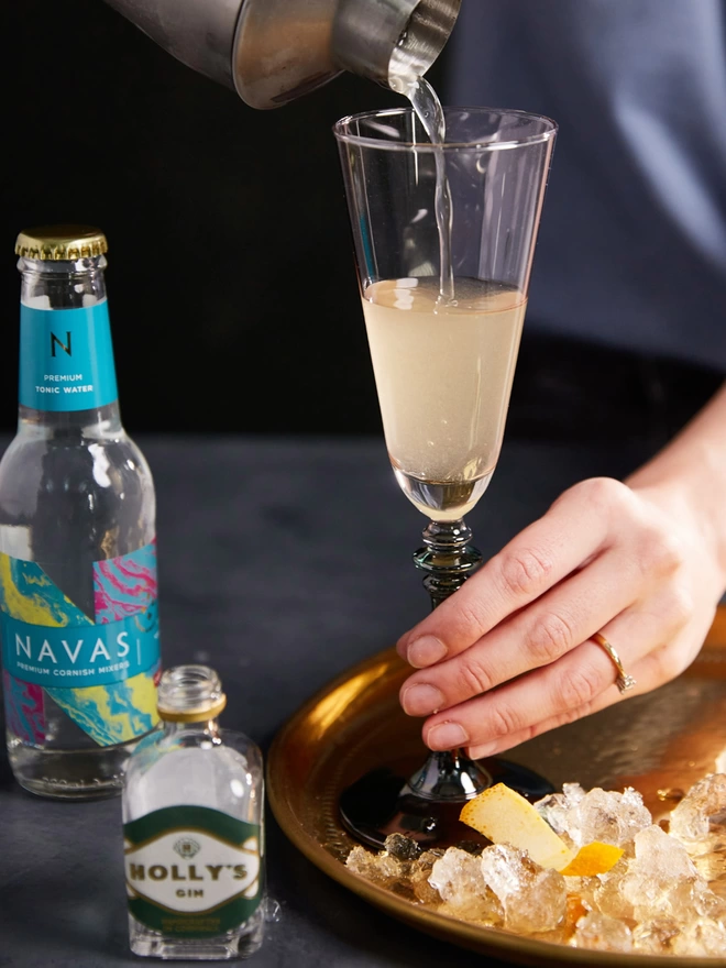 Pouring Holly's Gin cocktail from shaker into a champagne glass