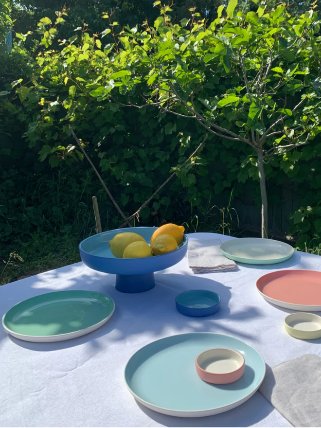 Fruit Stand. A table laid with plates and a blue and turquoise fruit.