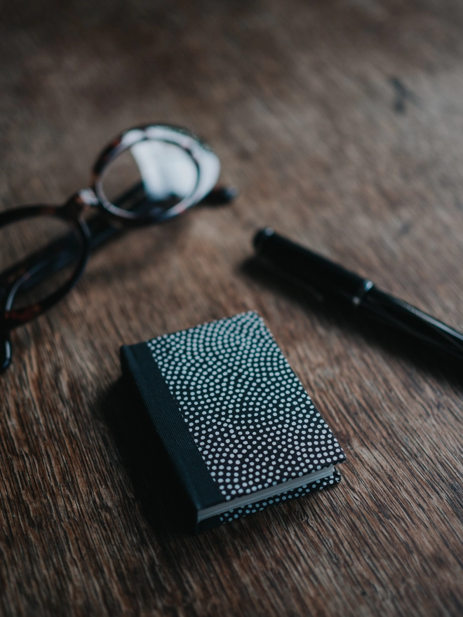 Black miniature book next to a pen and glasses