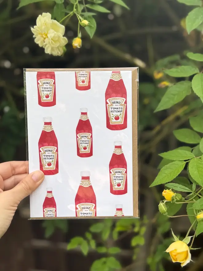 tomato ketchup bottles illustrated card. card. photographed against rosebush background.
