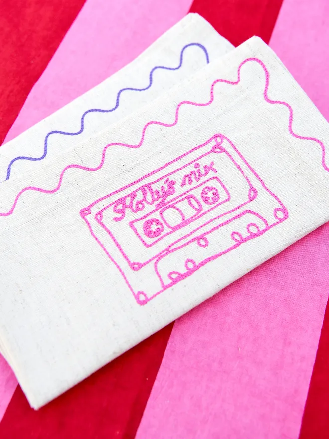 Personalised Cassette Embroidered Napkin personalised with 'Holly' on a striped red and pink tablecloth