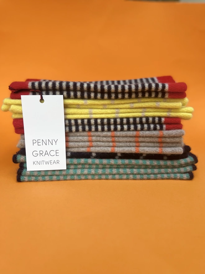 A pile of knitted striped wristwarmers on an orange background