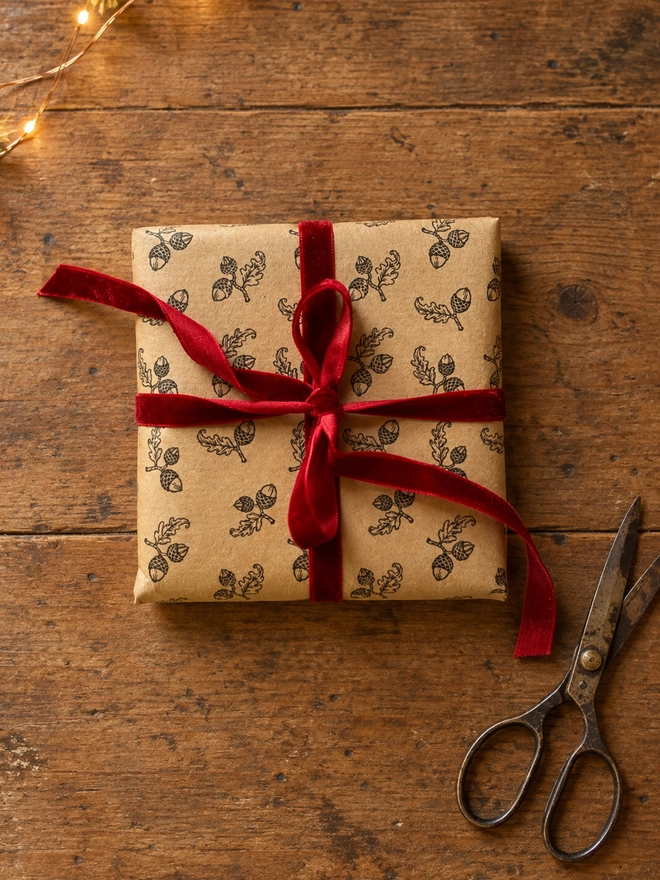 a square present wrapped in a hand stamped acorn kraft paper with a beautiful red ribbon tied in a bow