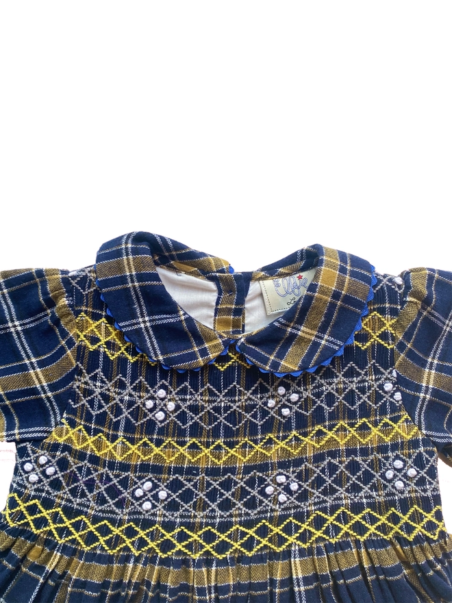 Detail of a navy and yellow tartan dress with hand smocked detail and a peter pan collar