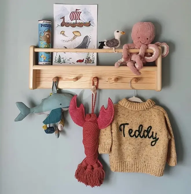 Personalised Cardigans, a brown cardigan personalised with a name hanging from a wooden shelf with lots of toys. 