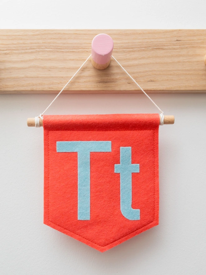 Coral pink banner with n upper and lowercase "T" in pale blue felt