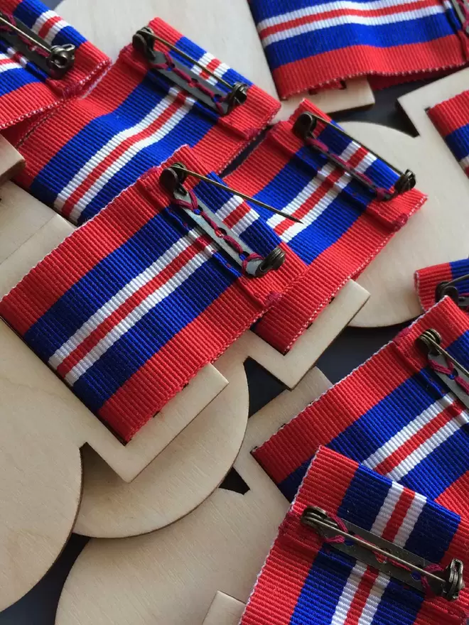 The backs of the medals are shown, pins are hand securely stitched onto red, white and blue ribbon