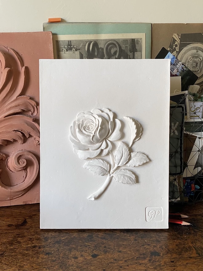 Decorative plaster wall plaque with Old Garden Rose design on a table with scrapbook and maquette behind
