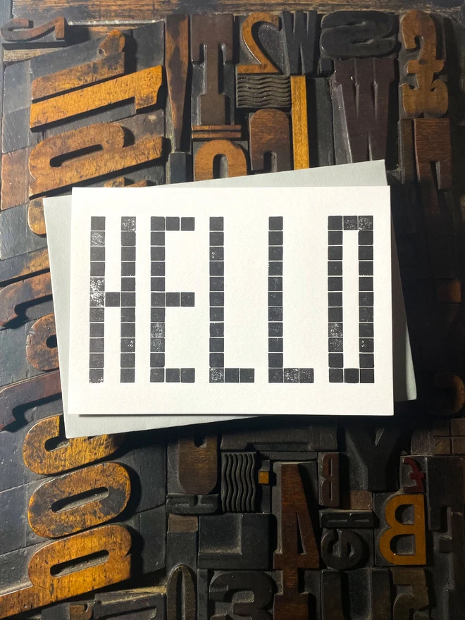 Letterpress HELLO postcard printed from a grid of square wooden type blocks in rich black ink, deeply impressed on thick 350gsm Colorplan Pristine White card.