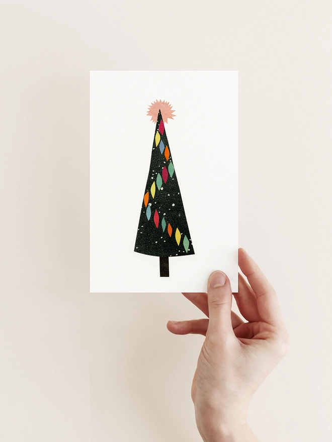 A mid century style greeting card featuring a black christmas tree decorated with colourful baubles and a pink star.